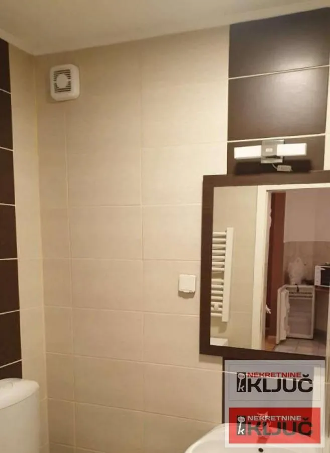 Pogled na kupatilo sa lavaboom, ogledalom i keramičkim pločicama.