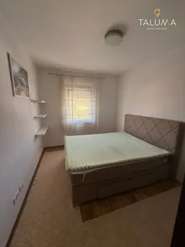 Manja spavaća soba sa bračnim krevetom, bijelim zidovima i prozorom sa zavjesom. - image 2