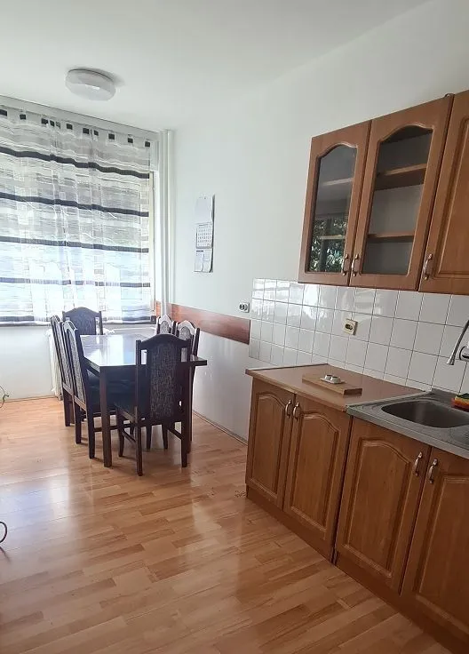 Kuhinja sa drvenim elementima i trpezarijskim stolom pored prozora.