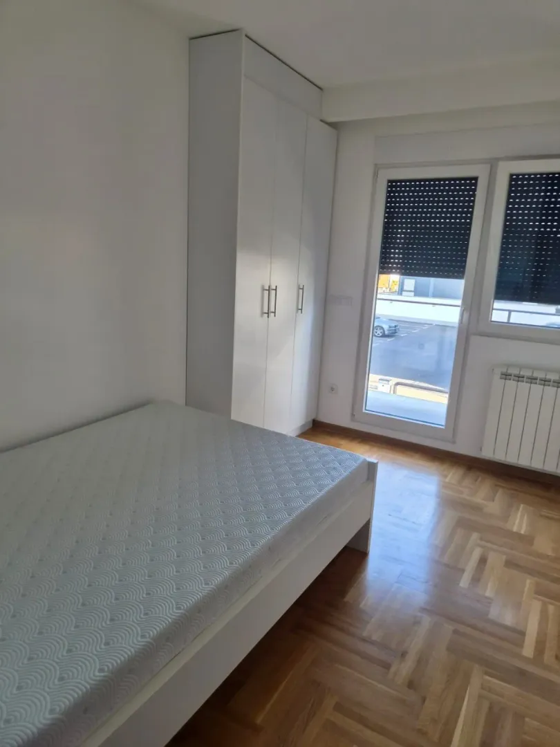 Svetla spavaća soba sa krevetom, belim garderoberom i parketom.