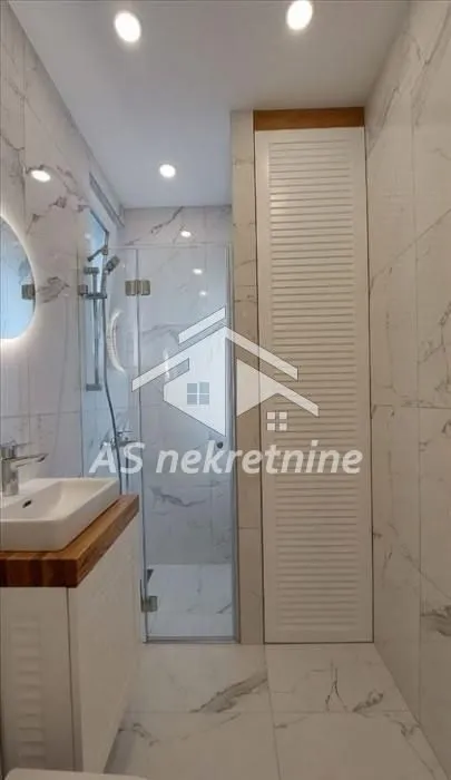 Moderno opremljeno kupatilo sa tuš kabinom i mermernim pločicama.