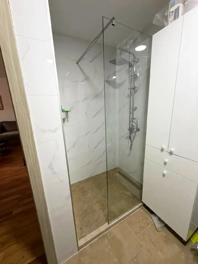 Moderne kupatilo sa tuš kabinom i bijelim elementima.