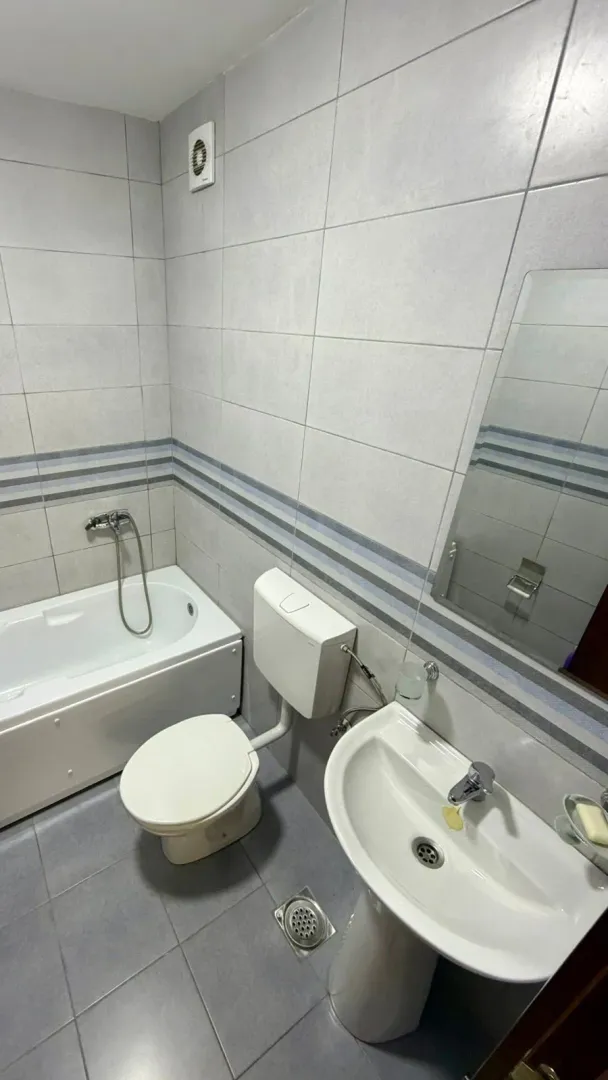 Kompaktno kupatilo sa kadom, umivaonikom i toaletom u sivo-bijelim tonovima.