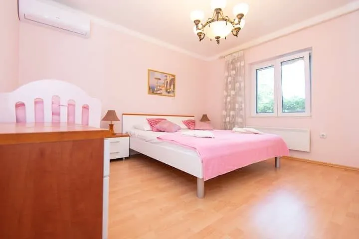 Prostrana spavaća soba sa bračnim krevetom, ružičastim detaljima i prozorom.