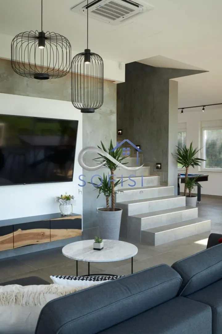 Modern living room with a television, sofa, and a staircase in the background.