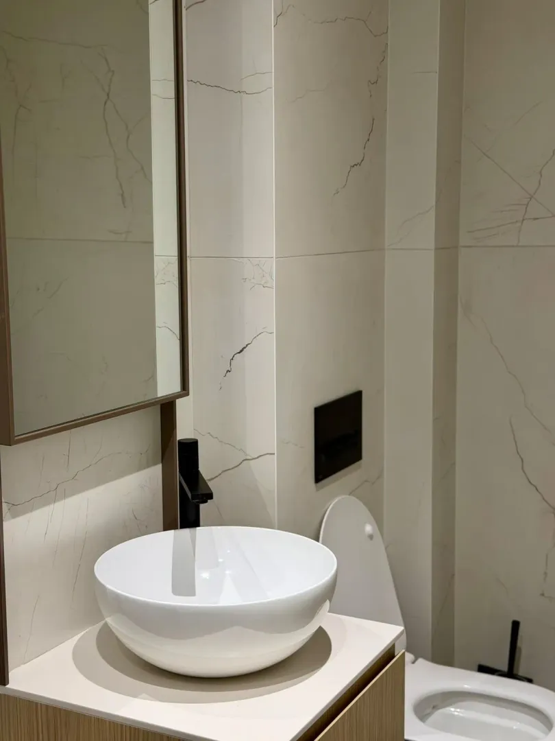 Modern bathroom with a basin, mirror, and toilet tiled with marble-effect tiles.