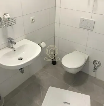 Manje kupatilo sa umivaonikom i toalet šoljom obloženo svetlim pločicama. - image 7