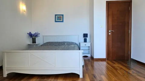 Spavaća soba sa bijelim krevetom, noćnim stočićem i drvenim podom. - image 7