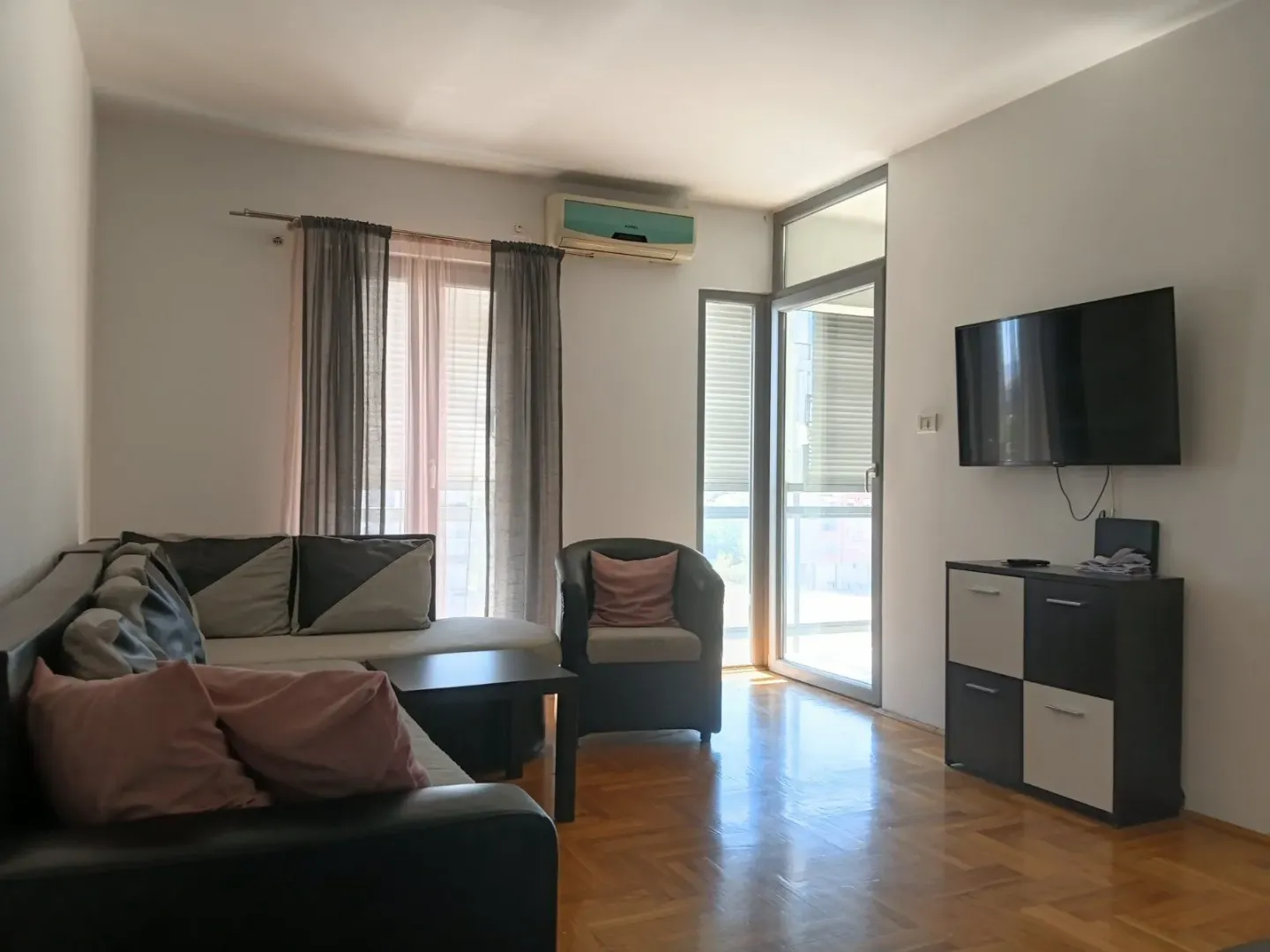 Dnevna soba sa garniturom, foteljom, TV komodom i izlazom na terasu.