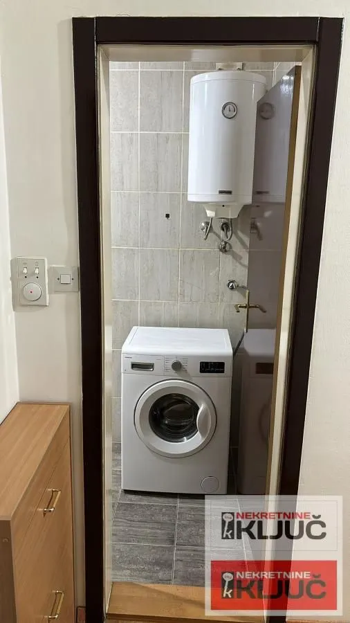 Pogled kroz vrata na kupatilo sa veš mašinom i bojlerom.