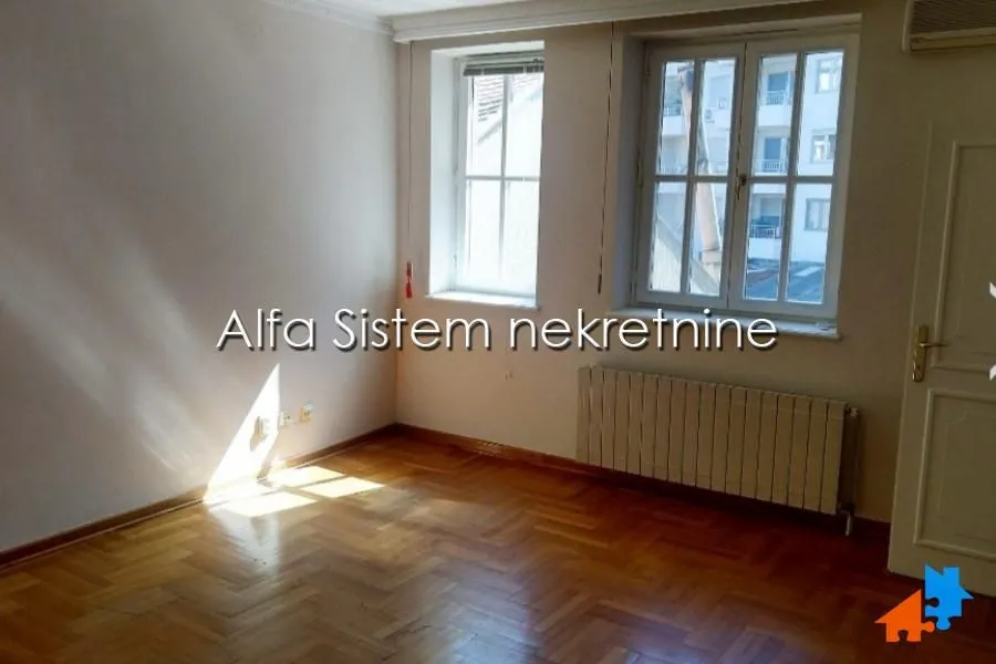 Empty room with hardwood flooring and two windows.