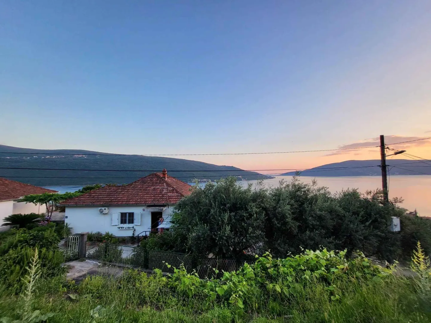 Pogled na kuću sa krovom od crijepa u okruženju zelenila i sa pogledom na more.