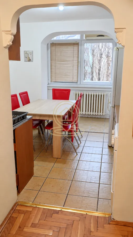 Kuhinja sa trpezarijom i crvenim stolicama, gledana kroz luk.