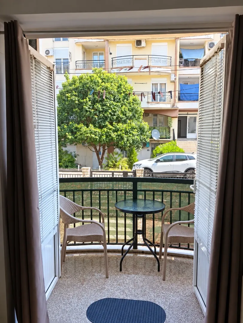 Namješten balkon sa stolom i stolicama i pogledom na dvorište i okolne zgrade.