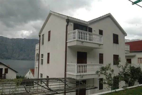 Trospratna kuća sa bijelom fasadom i balkonima u blizini mora.