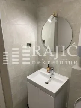 Manje kupatilo sa umivaonikom, ogledalom i svetlim pločicama. - image 8