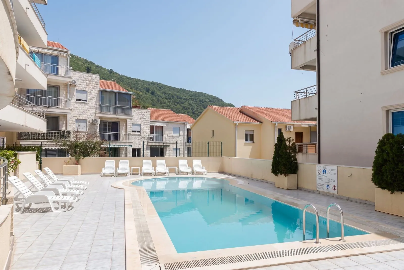 Outdoor swimming pool with sun loungers surrounded by residential buildings.