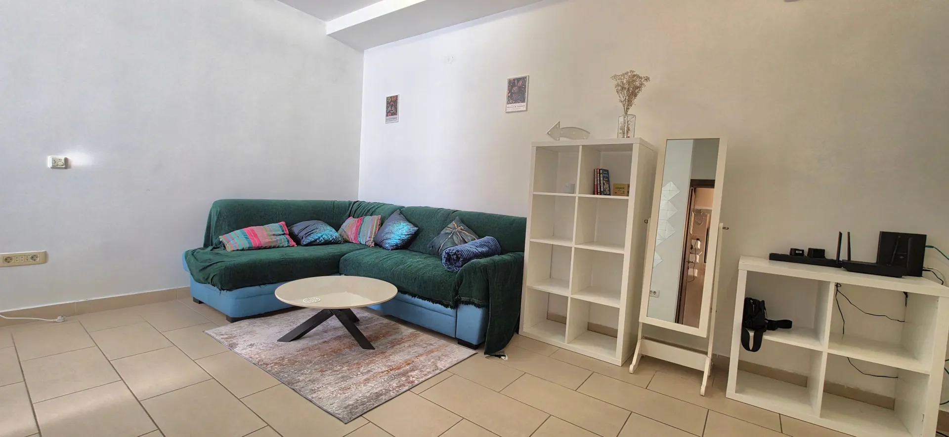 Living room with a green sectional sofa, coffee table and white shelving units.