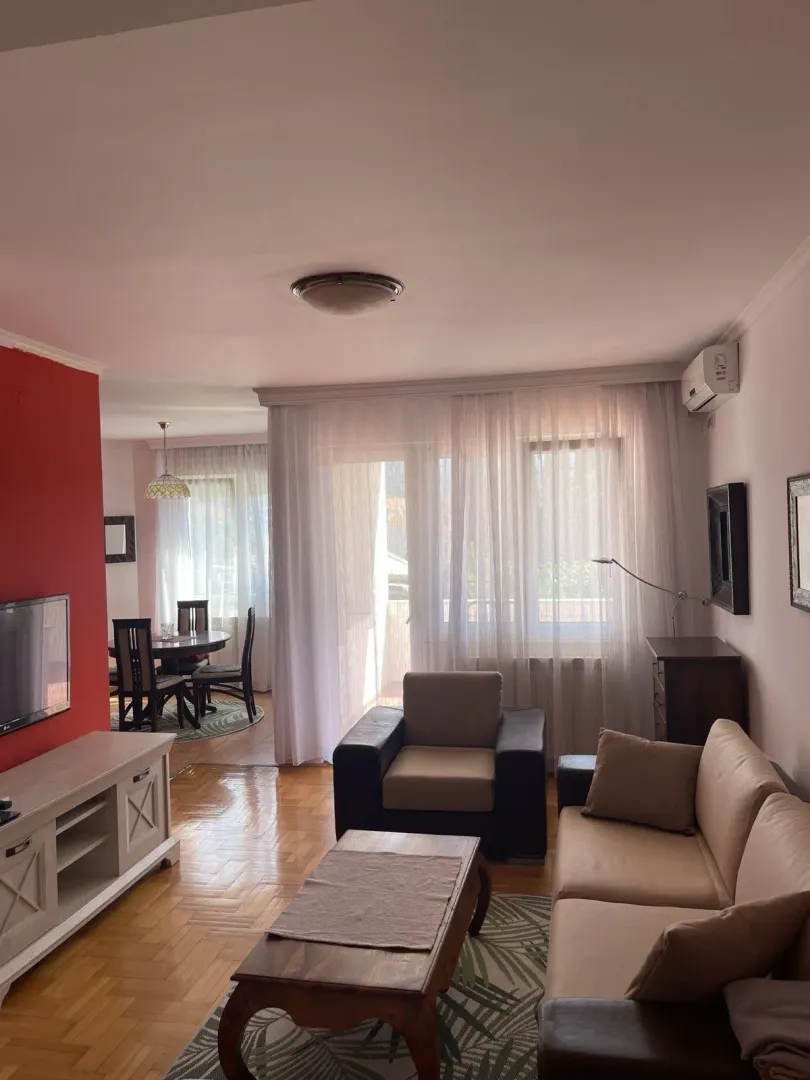 Bright living room with a seating area and dining space in the background.