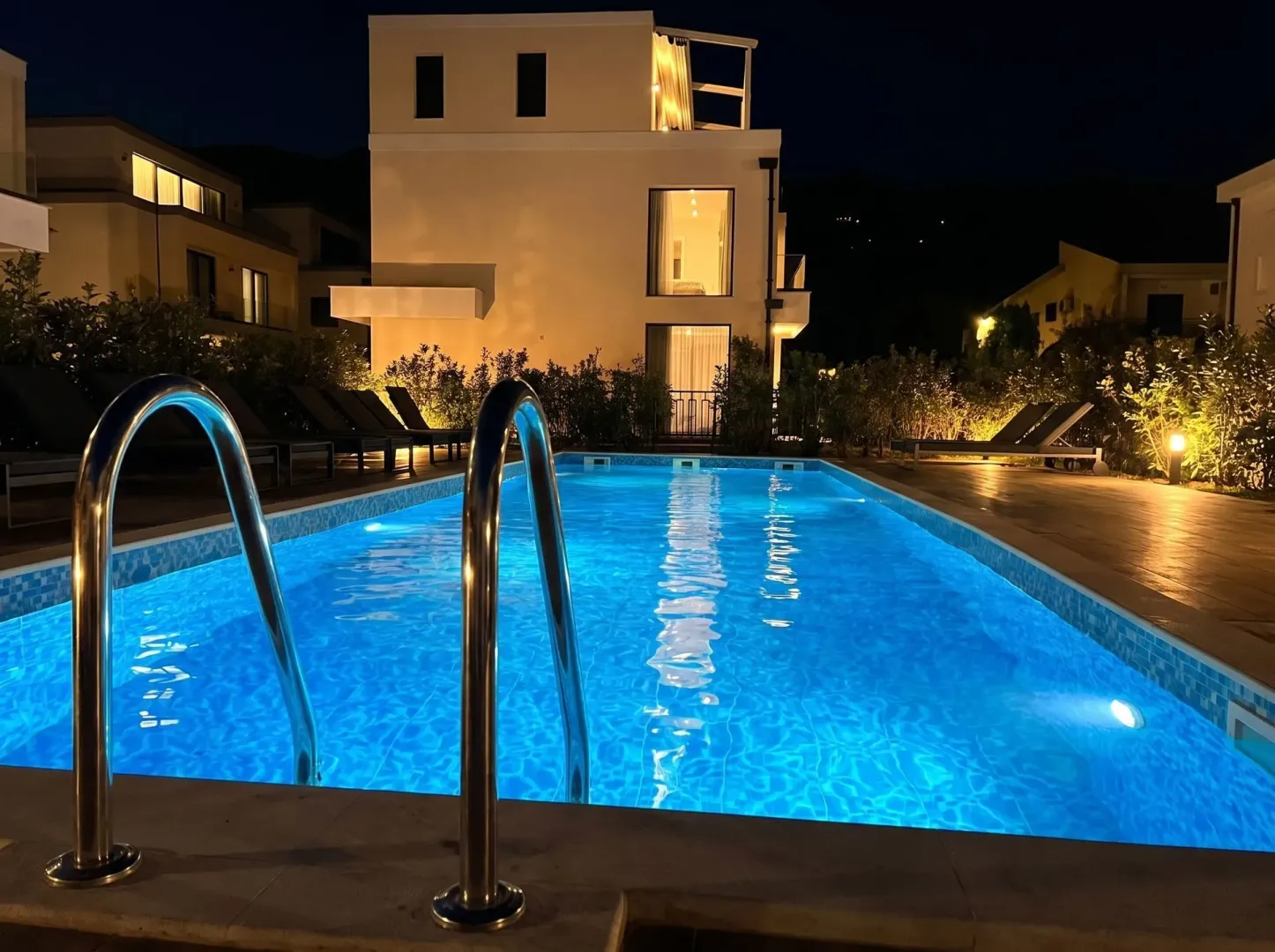 Osvijetljeni bazen u dvorištu vile noću sa pogledom na kuću.