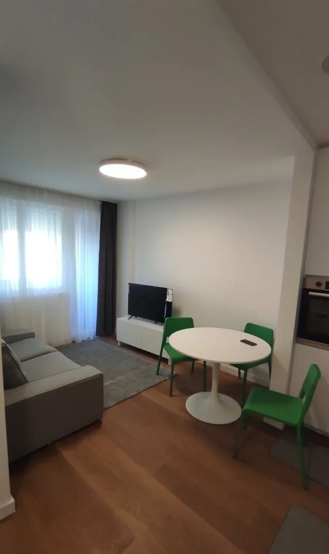 Dnevni boravak sa garniturom, trpezarijskim stolom i zelenim stolicama.