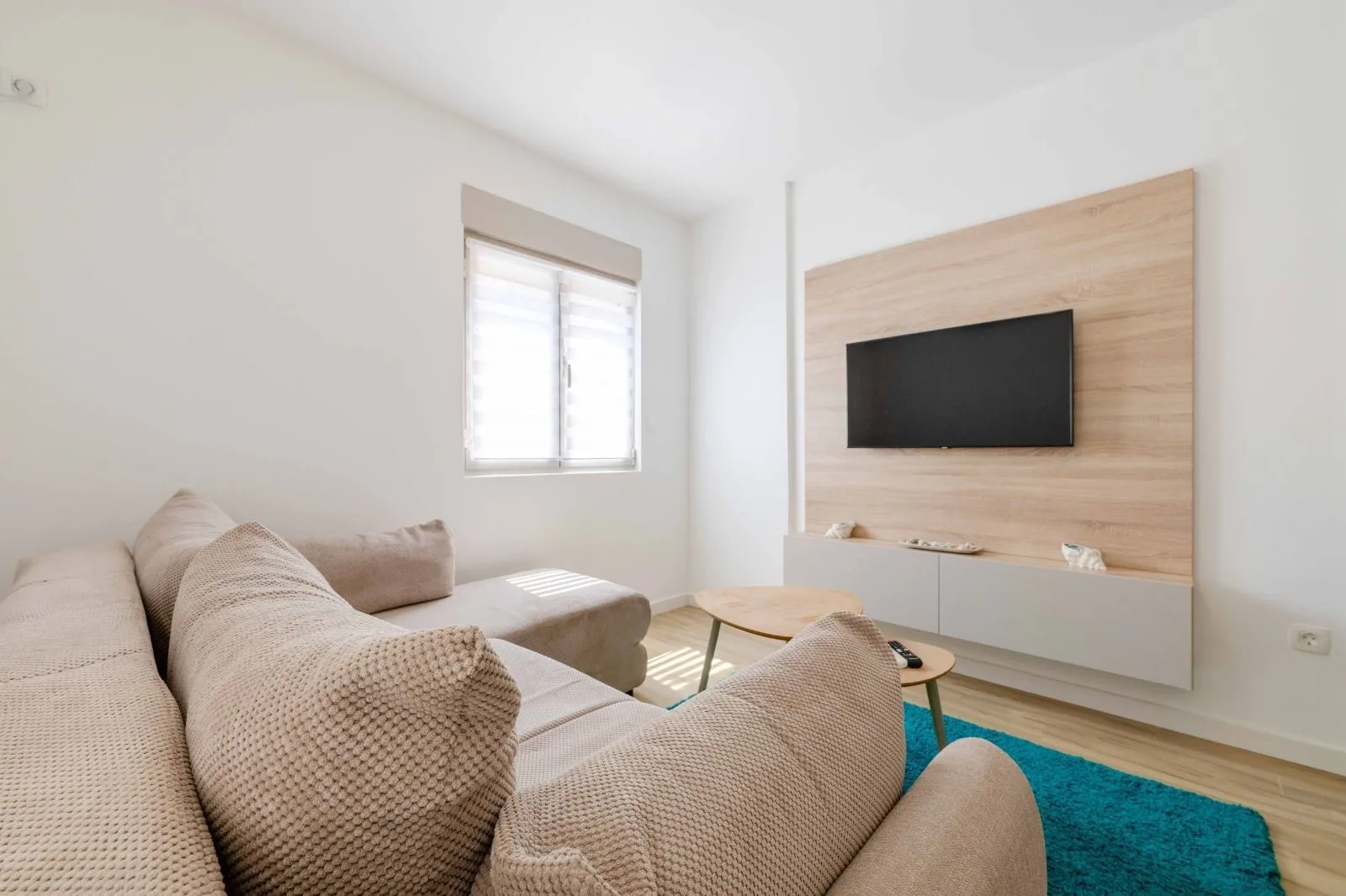 Living room with a sectional sofa, wall-mounted TV, and a window.