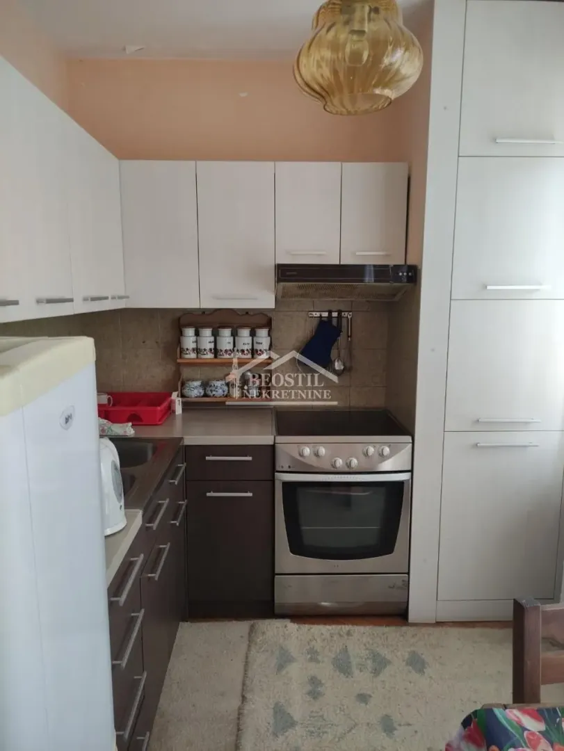 Manja kuhinja sa belim i tamnim elementima i šporetom.