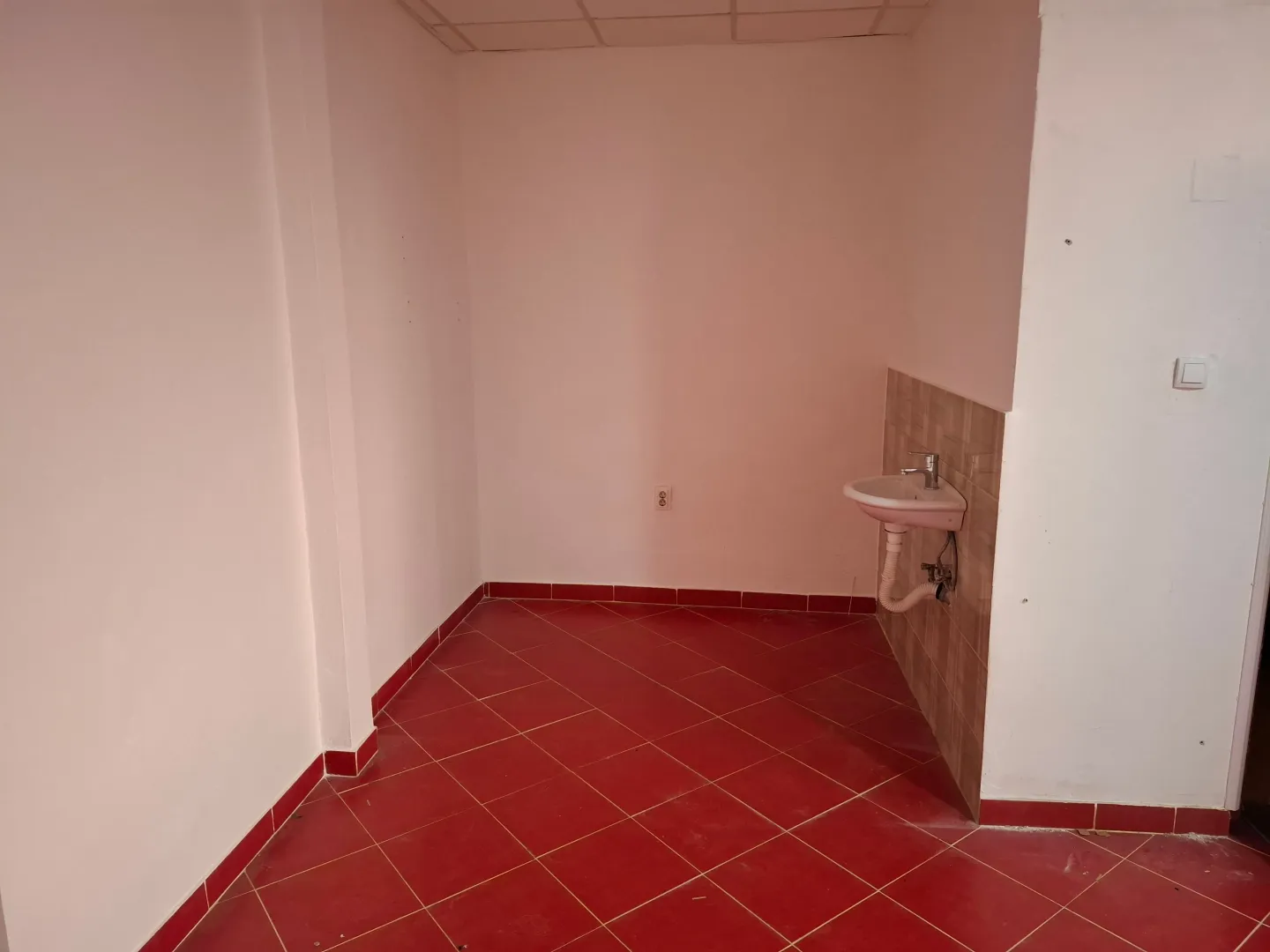 Small bathroom with a sink and red ceramic floor tiles.