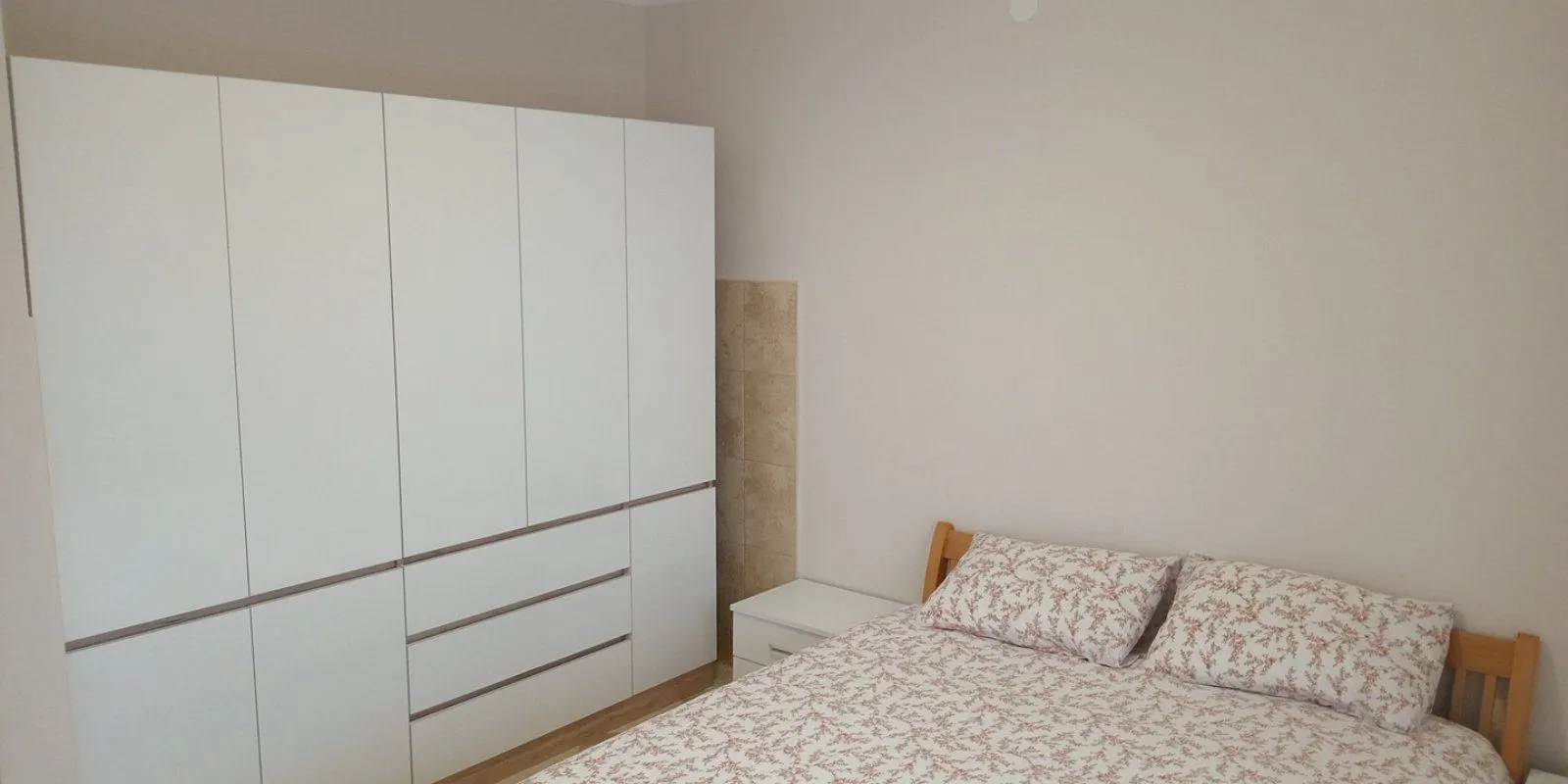Furnished bedroom with a bed and a large white wardrobe.
