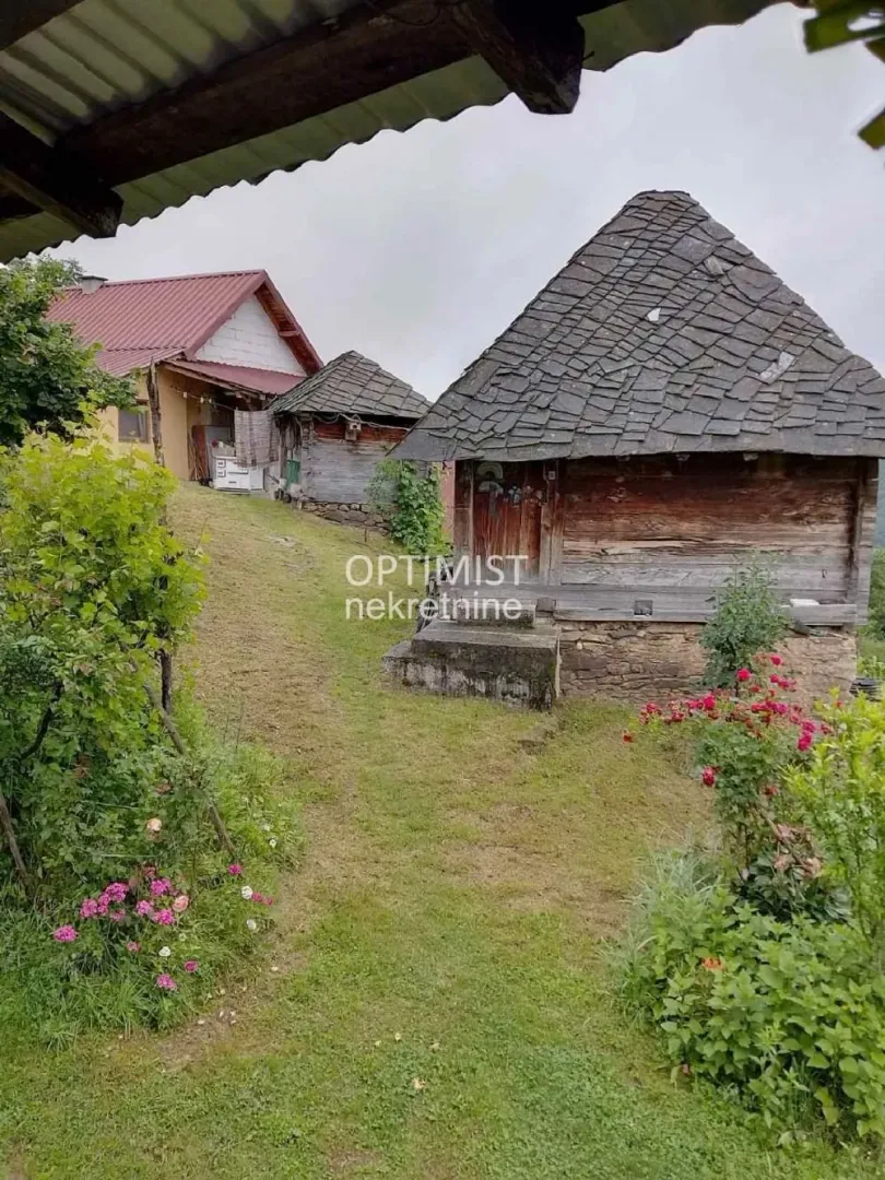 Pogled na dvorište sa starim drvenim kućicama i zelenilom.