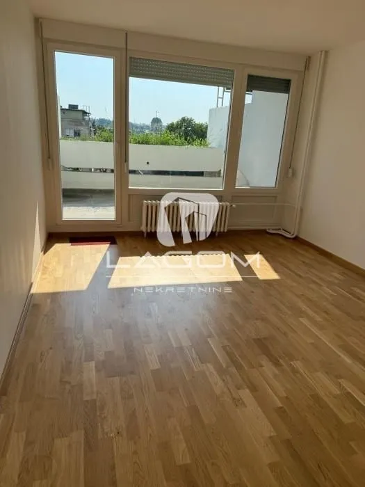 Prazna soba sa drvenim podom i velikim prozorima koji izlaze na terasu.