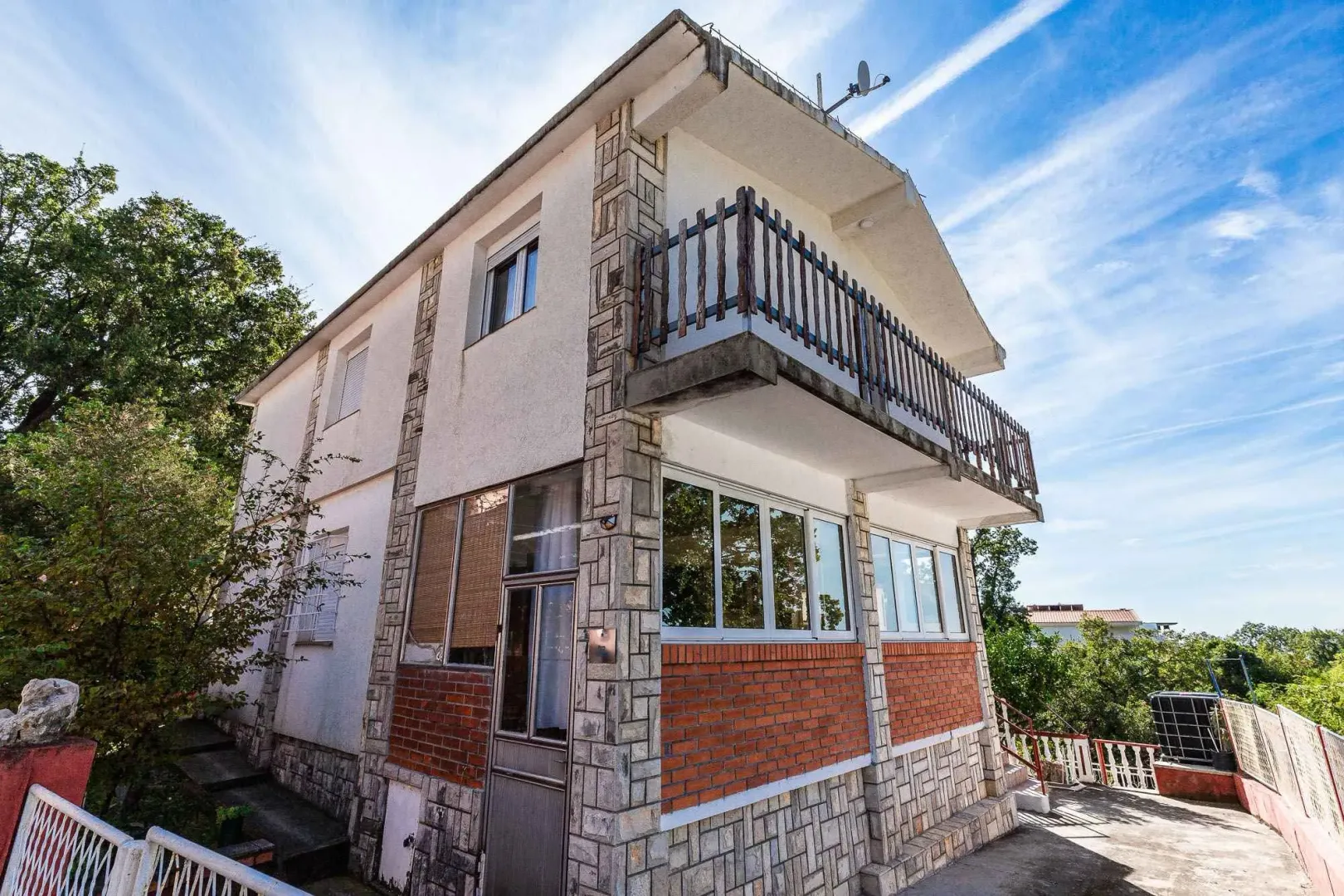 Eksterijer dvospratne kuće sa balkonom i kamenim detaljima.