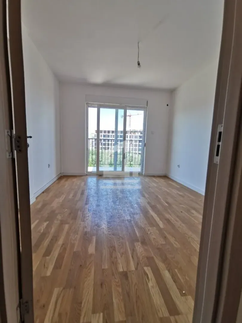 Empty room with wooden flooring and balcony doors.