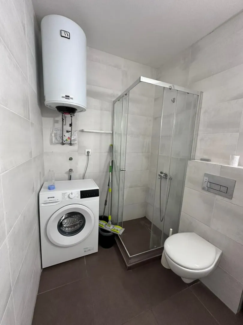 Smaller bathroom equipped with a shower cabin, toilet, washing machine, and water heater.