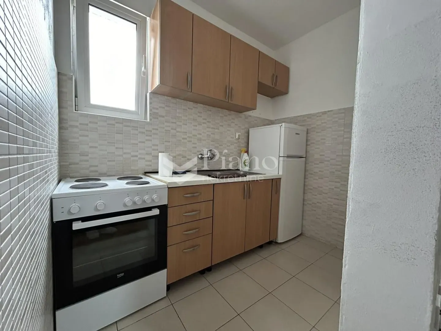 Small kitchen with wooden units, cooker and refrigerator.