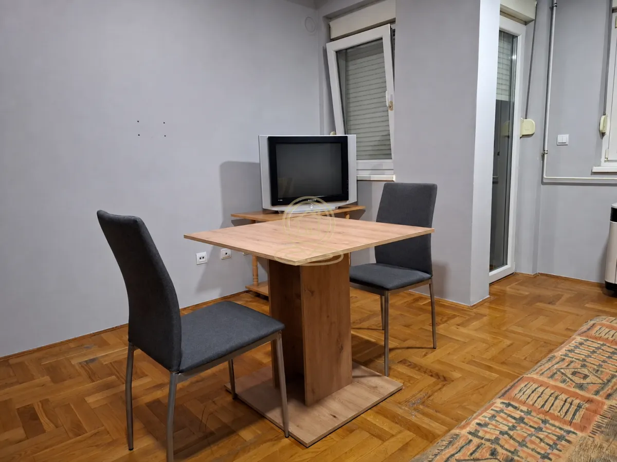 Manji trpezarijski sto sa dve stolice i televizorom u dnevnom boravku.