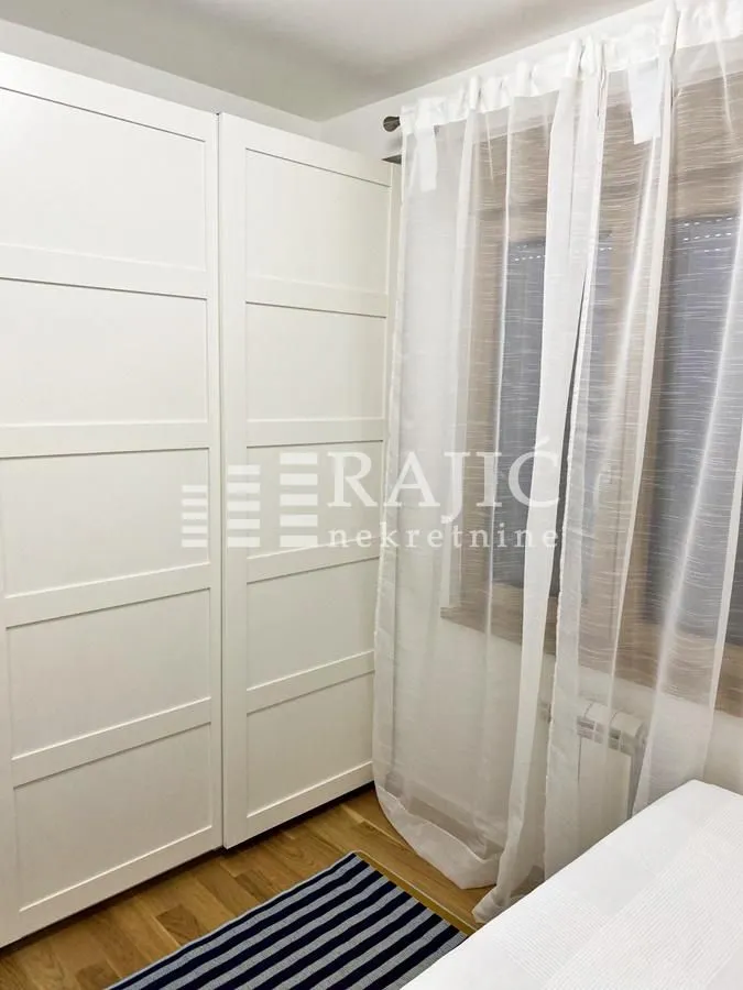 Bedroom with a white wardrobe and a window with curtains.