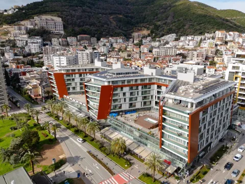 Pogled iz vazduha na moderan stambeno-poslovni kompleks sa uređenom okolinom i gradom u pozadini. - image 8