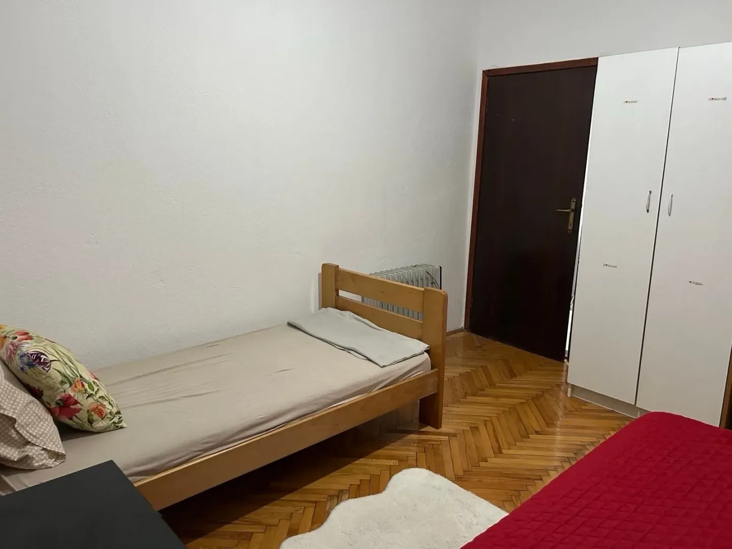 Small bedroom with a wooden bed, wardrobe, and parquet flooring.