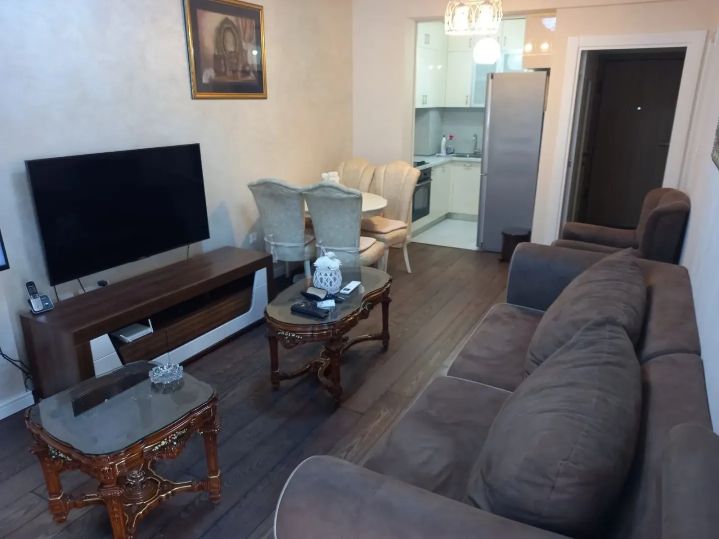 Living room with sofa, TV, and dining table, with a view of the kitchen.