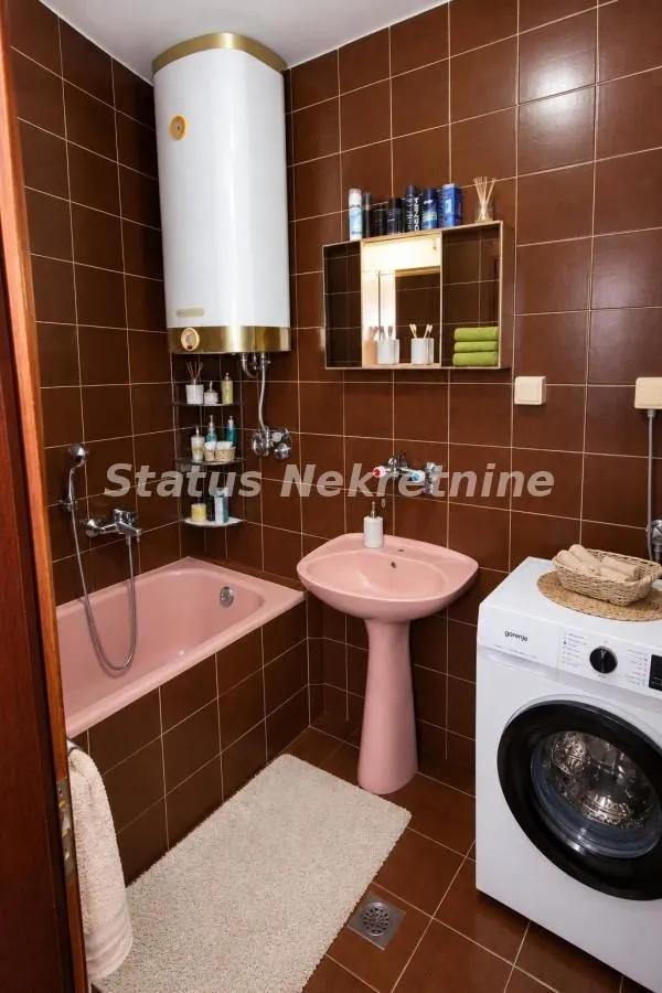 Kupatilo obloženo smeđim pločicama sa pink kadom, lavaboom i veš mašinom.