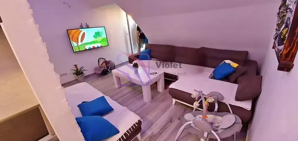 Dnevna soba sa garniturom, stočićem i televizorom na zidu.