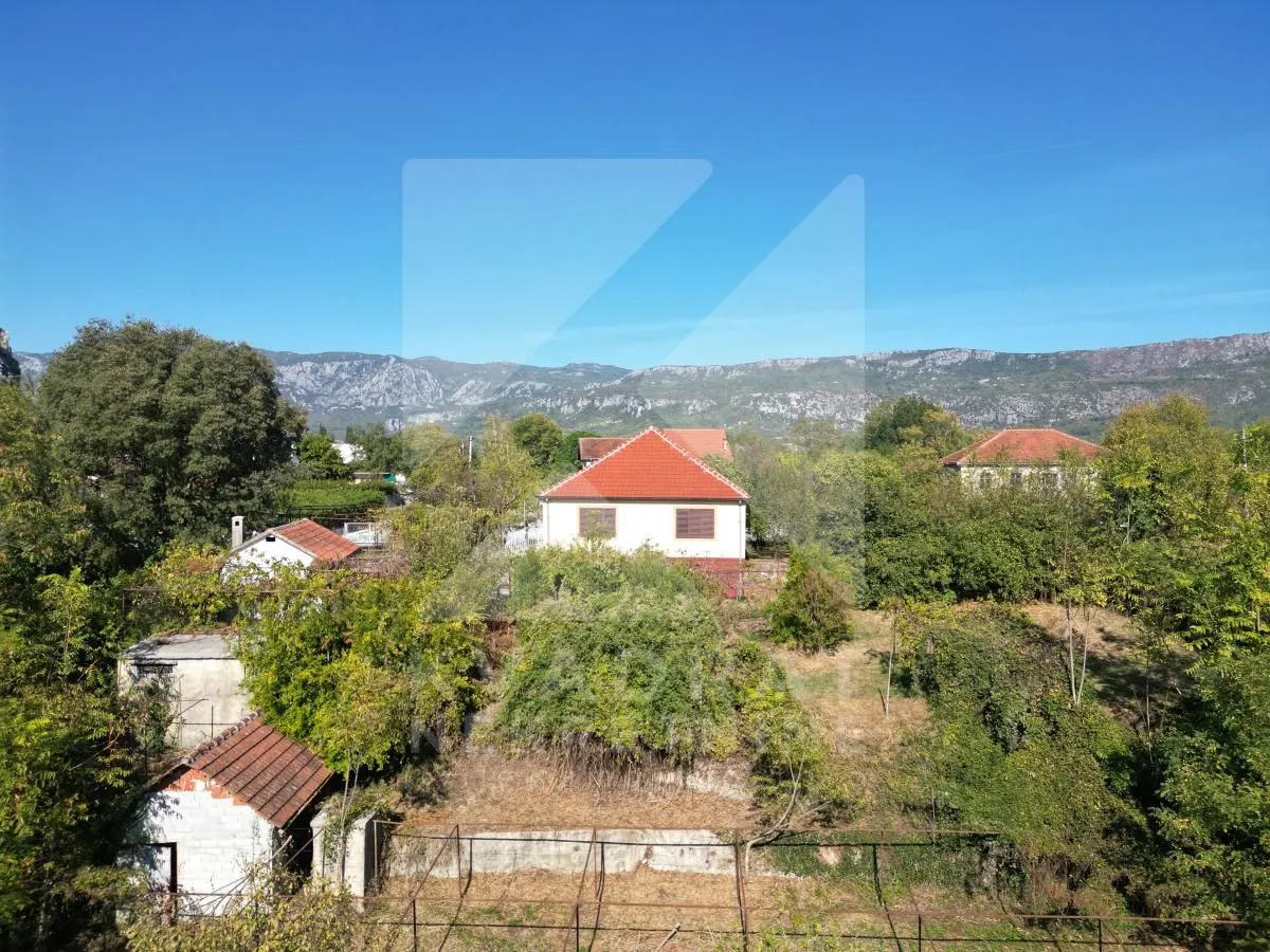 Pogled na kuću i imanje okruženo zelenilom i planinama u pozadini.