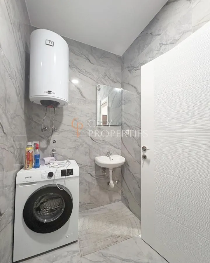 Bathroom tiled in marble-effect tiles featuring a washing machine, water heater, and washbasin.
