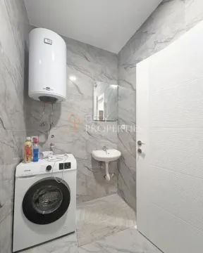 Bathroom tiled in marble-effect tiles featuring a washing machine, water heater, and washbasin. - image 12