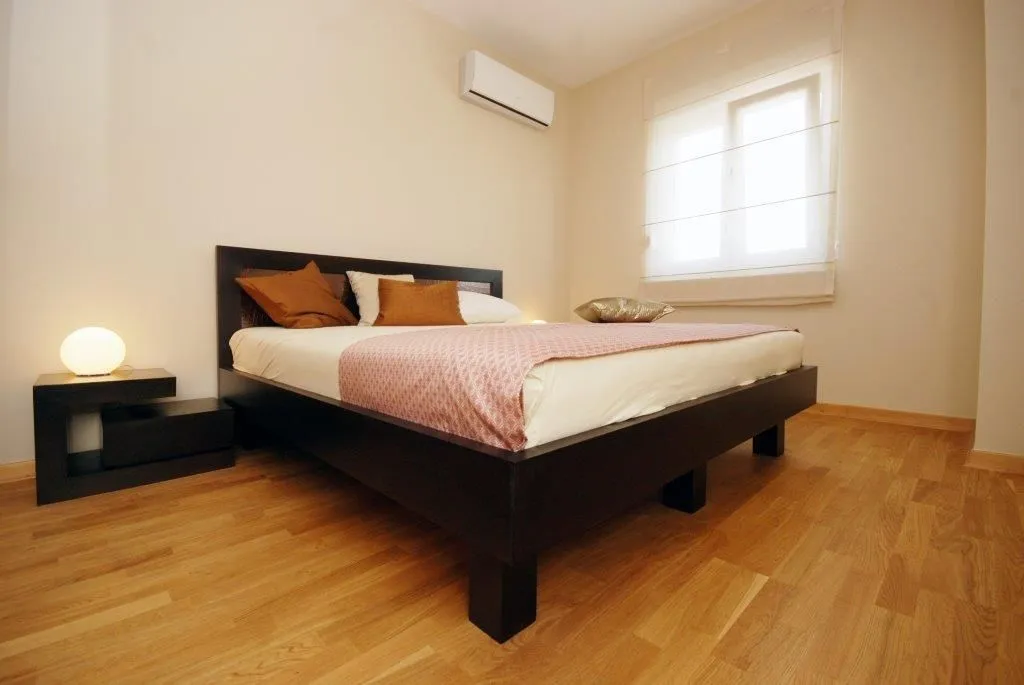 A bright bedroom featuring a dark wooden double bed and an air conditioning unit.