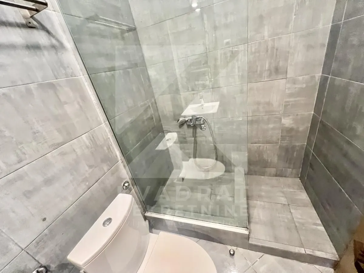 Kupatilo sa tuš kabinom od stakla i sanitarijama u sivim pločicama.