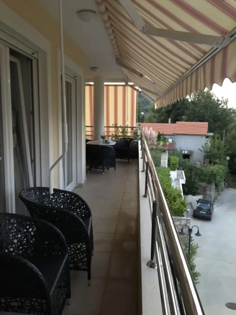 Prostrana natkrivena terasa sa garniturom za sjedenje i tendom.