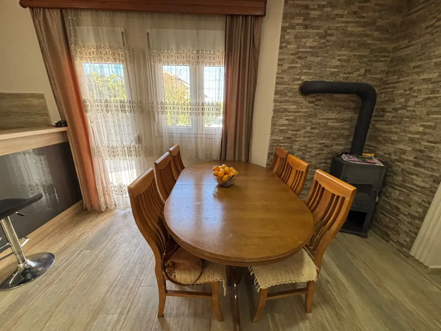 Dining area with a wooden table, chairs, and a wood-burning stove next to a brick wall.