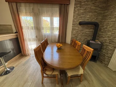 Dining area with a wooden table, chairs, and a wood-burning stove next to a brick wall. - image 6